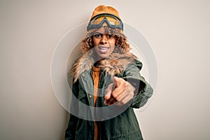 Young african american skier woman with curly hair wearing snow sportswear and ski goggles pointing displeased and frustrated to