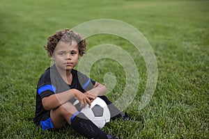Young African American soccer player sitting on a grass field expressionless before a soccer game photo