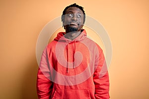 Young african american sporty man wearing sweatshirt with hoodie over yellow background looking away to side with smile on face,