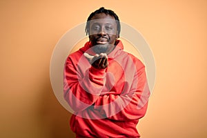 Young african american sporty man wearing sweatshirt with hoodie over yellow background looking at the camera blowing a kiss with