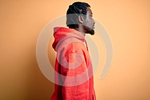 Young african american sporty man wearing sweatshirt with hoodie over yellow background looking to side, relax profile pose with
