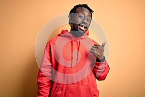 Young african american sporty man wearing sweatshirt with hoodie over yellow background smiling with happy face looking and