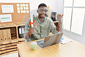 Young african american student man holding graduate degree diploma sitting on the table pointing thumb up to the side smiling