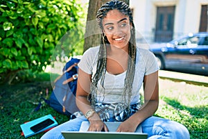 Young african american student woman smiling happy using computer laptop sitting on the grass at the university campus