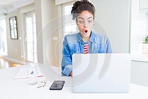 Young african american student woman using computer laptop scared in shock with a surprise face, afraid and excited with fear