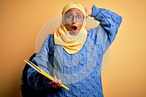 Young African American student woman wearing muslim hijab and backpack holding book Crazy and scared with hands on head, afraid