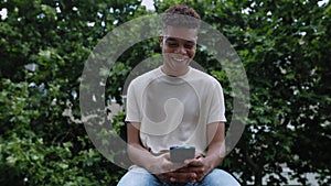 Young african american teenager boy using mobile phone while sitting outdoor