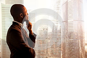 Young african-american thoughtful businessman looking through wi