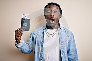 Young african american tourist man holding passport with dollars banknotes as money travel scared in shock with a surprise face,