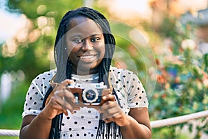 Young african american tourist woman smiling happy using vintage camera at the city