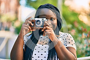 Young african american tourist woman smiling happy using vintage camera at the city