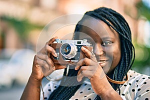 Young african american tourist woman smiling happy using vintage camera at the city