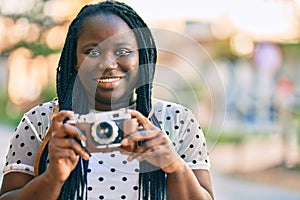 Young african american tourist woman smiling happy using vintage camera at the city