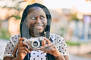 Young african american tourist woman smiling happy using vintage camera at the city