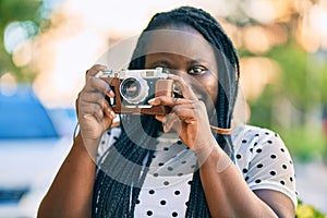 Young african american tourist woman smiling happy using vintage camera at the city