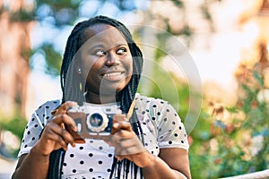 Young african american tourist woman smiling happy using vintage camera at the city