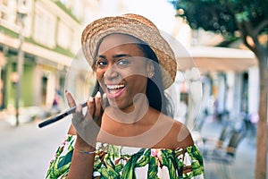 Young african american tourist woman on vacation smiling happy sending voice message using smartphone at the city