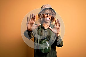 Young african american tourist woman on vacation wearing explorer hat and water canteen afraid and terrified with fear expression