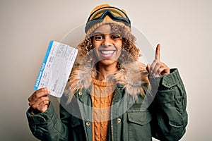 Young african american tourist woman wearing ski goggles holding plane boarding pass tickets surprised with an idea or question