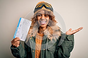 Young african american tourist woman wearing ski goggles holding plane boarding pass tickets very happy and excited, winner