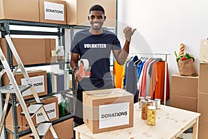 Young african american volunteer man packing donations box for charity pointing to the back behind with hand and thumbs up,