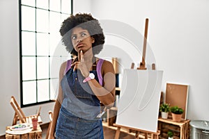 Young african american woman with afro hair at art studio thinking concentrated about doubt with finger on chin and looking up