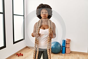 Young african american woman with afro hair at the gym training with battle ropes puffing cheeks with funny face