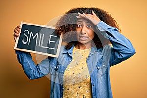 Young african american woman with afro hair holding blackboard with smile message stressed with hand on head, shocked with shame