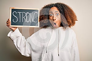 Young african american woman with afro hair holding blackboard with strong message scared in shock with a surprise face, afraid