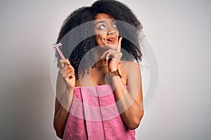 Young african american woman with afro hair in a towel holding female razor for body depilation serious face thinking about