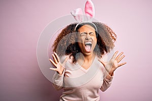 Young african american woman with afro hair wearing bunny ears over pink background celebrating mad and crazy for success with