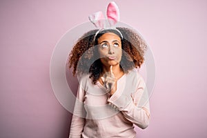 Young african american woman with afro hair wearing bunny ears over pink background Thinking concentrated about doubt with finger