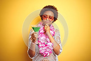 Young african american woman with afro hair wearing flower hawaiian lei and drinking a cocktail serious face thinking about