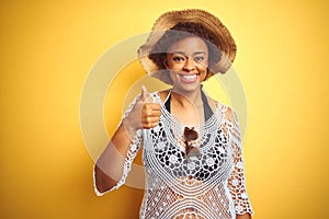 Young african american woman with afro hair wearing summer hat over white isolated background doing happy thumbs up gesture with