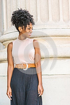 Young African American woman with afro hairstyle, white ear bead pin, wearing sleeveless light color top, dark orange belt, black