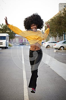 Young African American woman with afro jumps, looking to camera, while crossing street, front view, vertical