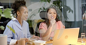 Young African American woman and biracial woman collaborate in a business office setting