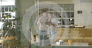 Young African American woman and biracial woman discuss over a tablet in a business office setting