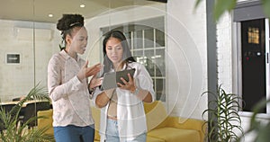 Young African American woman and biracial woman discuss a tablet in a business office setting