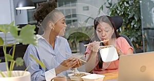 Young African American woman and biracial woman enjoy a business meal at the office