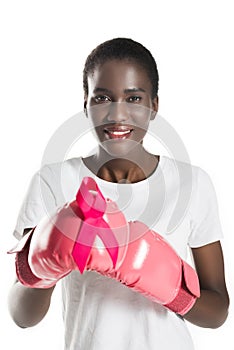 young african american woman in boxing gloves holding pink ribbon and smiling at camera