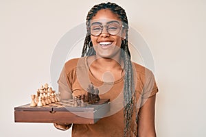 Young african american woman with braids holding chess board wearing glasses smiling and laughing hard out loud because funny