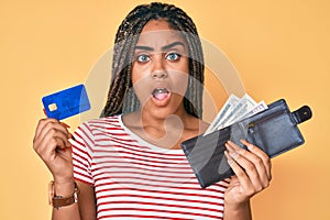 Young african american woman with braids holding wallet with dollars and credit card afraid and shocked with surprise and amazed