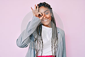 Young african american woman with braids wearing business jacket smiling happy doing ok sign with hand on eye looking through