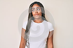 Young african american woman with braids wearing casual white tshirt smiling looking to the side and staring away thinking