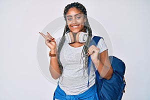 Young african american woman with braids wearing student backpack and headphones smiling happy pointing with hand and finger to