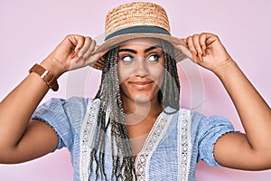 Young african american woman with braids wearing summer hat smiling looking to the side and staring away thinking