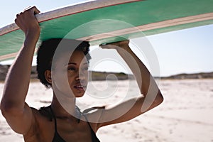 Young African American woman carrying the surfboard on her head at beach