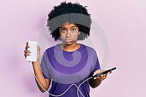 Young african american woman charging smartphone using portable battery skeptic and nervous, frowning upset because of problem