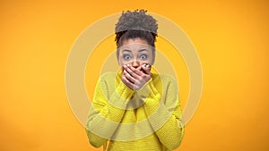 Young African-American woman closing mouth with hands, keeping secret, gossip